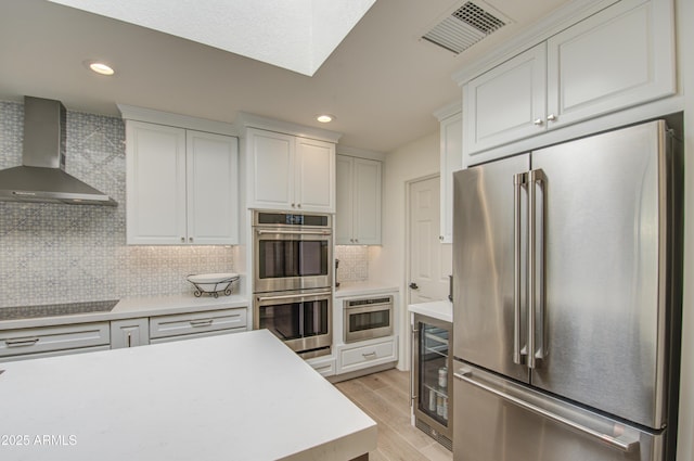 kitchen with stainless steel appliances, white cabinets, beverage cooler, and wall chimney exhaust hood