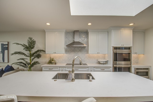 kitchen with sink, wall chimney range hood, backsplash, and double oven