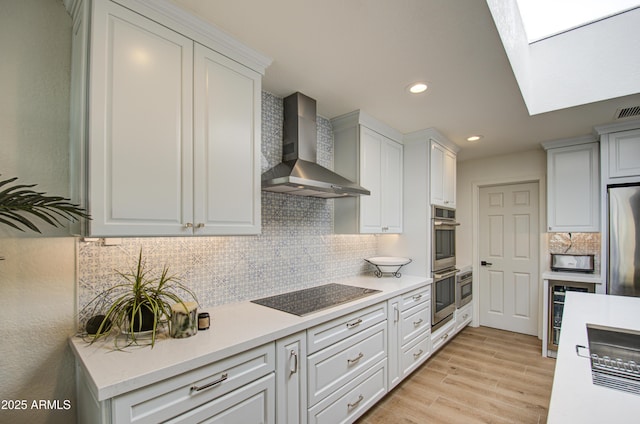 kitchen featuring stainless steel appliances, white cabinetry, and wall chimney range hood