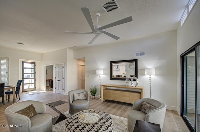 living room with a textured ceiling, light hardwood / wood-style floors, and ceiling fan
