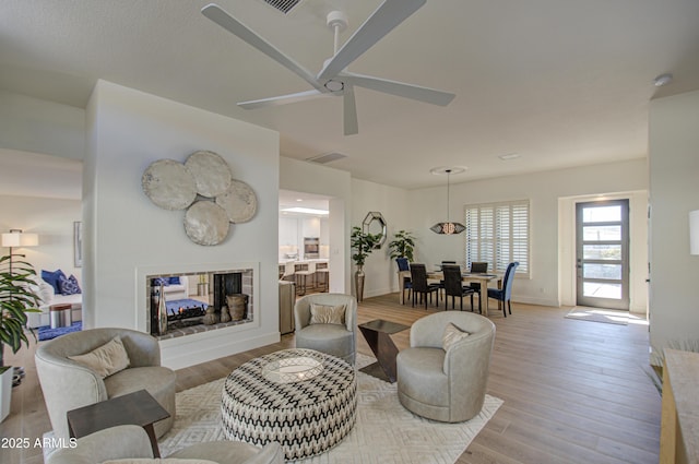 living room with light hardwood / wood-style flooring, ceiling fan, and a multi sided fireplace