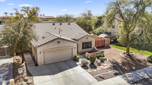 mediterranean / spanish-style home with an attached garage, fence, a tile roof, concrete driveway, and stucco siding