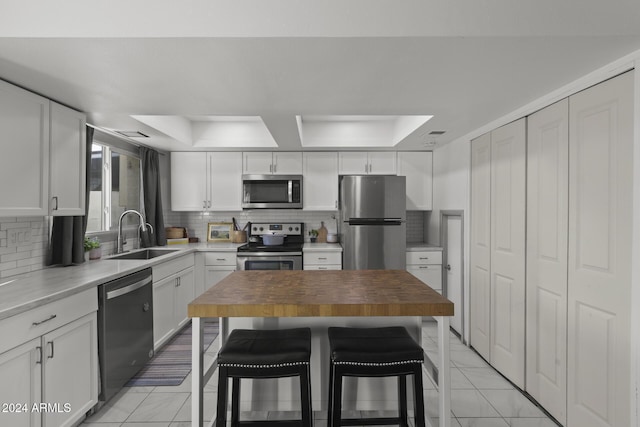 kitchen with wood counters, appliances with stainless steel finishes, a kitchen bar, sink, and white cabinetry