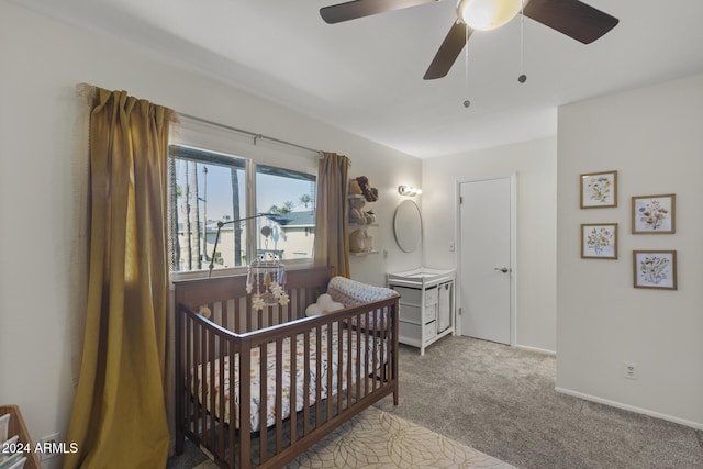 bedroom with a crib, light carpet, and ceiling fan