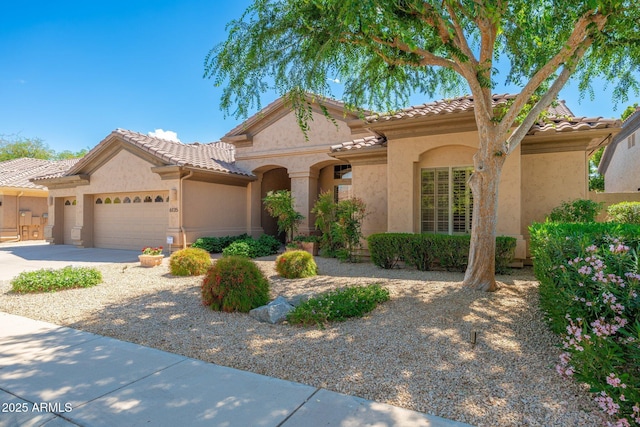 mediterranean / spanish house featuring an attached garage, driveway, a tile roof, and stucco siding