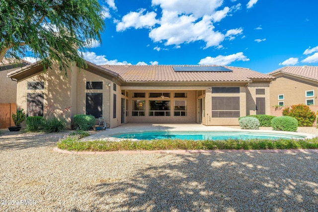 rear view of property featuring a patio, a tiled roof, solar panels, and stucco siding
