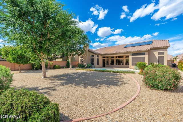 rear view of property featuring a tile roof, stucco siding, a sunroom, solar panels, and fence private yard