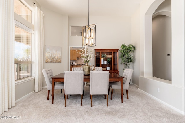 dining room with light colored carpet, arched walkways, baseboards, and an inviting chandelier