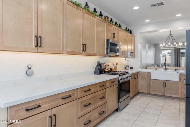 kitchen featuring visible vents, a sink, appliances with stainless steel finishes, light brown cabinetry, and light stone countertops