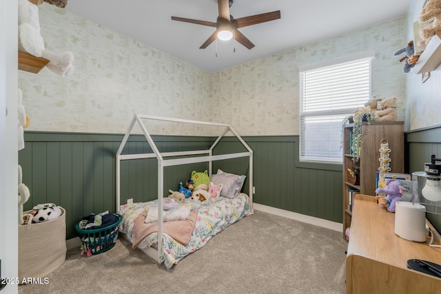 carpeted bedroom featuring wallpapered walls, a wainscoted wall, and ceiling fan
