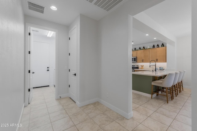 hall featuring baseboards, recessed lighting, light tile patterned floors, visible vents, and a sink