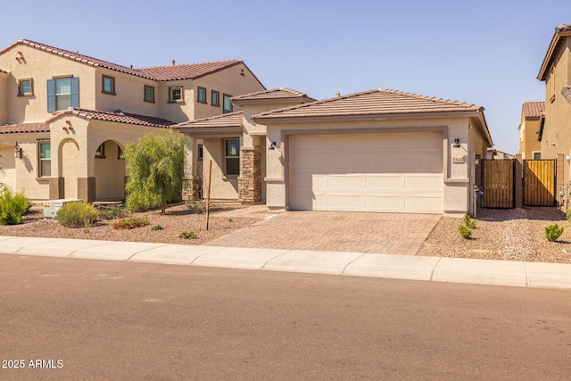 view of front of home featuring a tiled roof, stucco siding, decorative driveway, fence, and a garage
