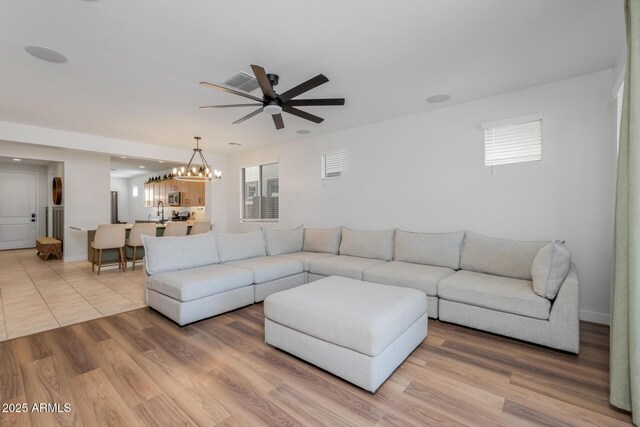 living area featuring plenty of natural light, visible vents, ceiling fan with notable chandelier, and baseboards