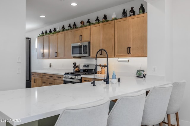 kitchen featuring recessed lighting, a peninsula, a kitchen bar, and appliances with stainless steel finishes