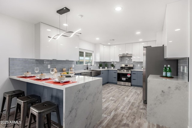 kitchen featuring a kitchen bar, stainless steel stove, white cabinets, kitchen peninsula, and pendant lighting