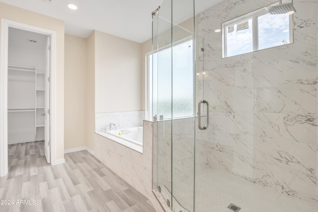 bathroom featuring a marble finish shower, a spacious closet, baseboards, wood finished floors, and a bath