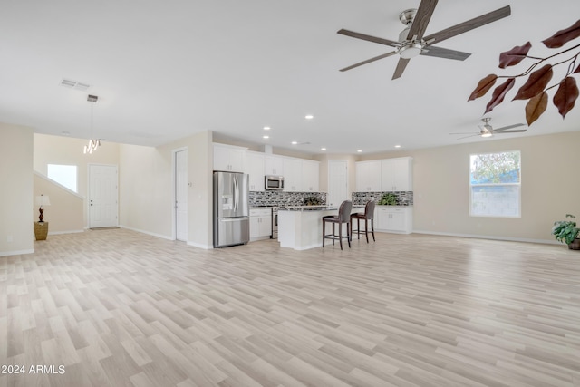 unfurnished living room featuring ceiling fan with notable chandelier and light hardwood / wood-style floors