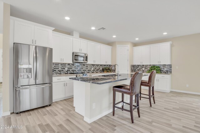 kitchen with white cabinetry, stainless steel appliances, dark stone counters, and light hardwood / wood-style flooring