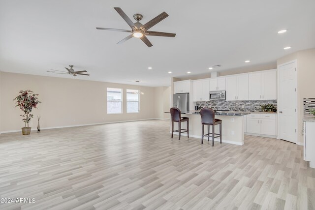 kitchen with light wood-type flooring, appliances with stainless steel finishes, an island with sink, and ceiling fan