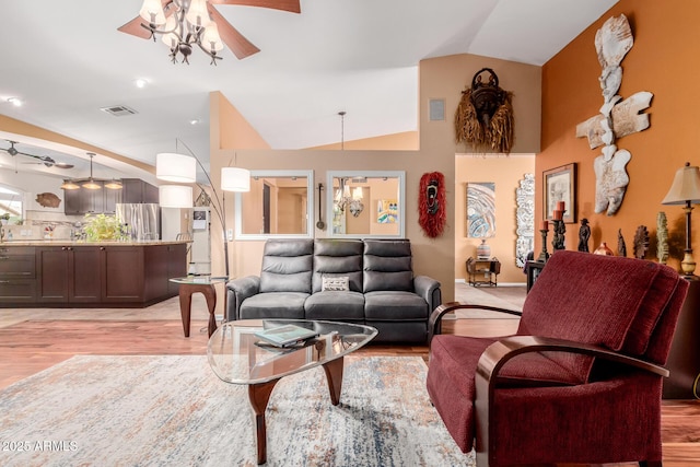 living room with vaulted ceiling, ceiling fan with notable chandelier, and light wood-type flooring