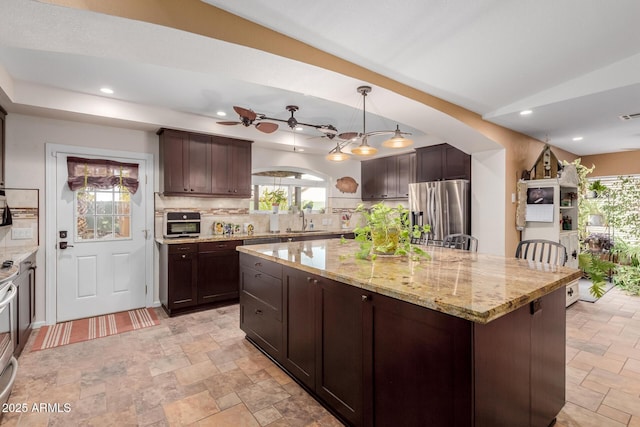 kitchen featuring stainless steel refrigerator with ice dispenser, light stone counters, decorative light fixtures, a kitchen island, and backsplash