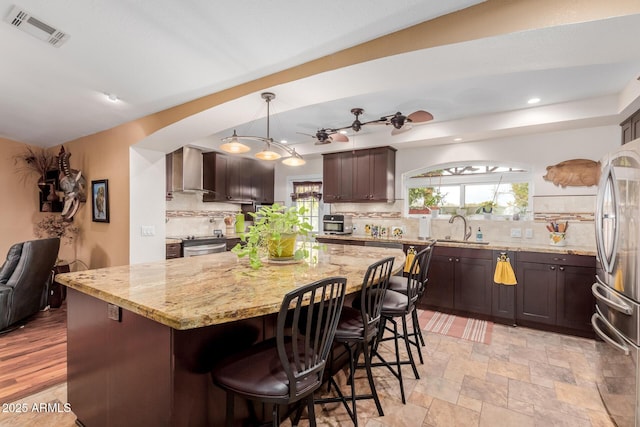 kitchen featuring pendant lighting, wall chimney range hood, sink, stainless steel appliances, and a center island