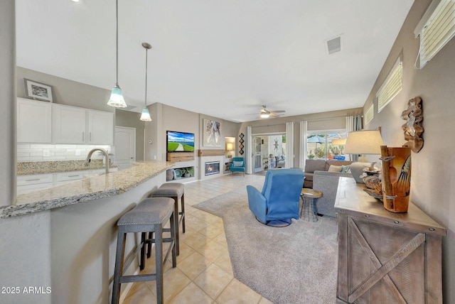 living room featuring light tile patterned floors, a glass covered fireplace, visible vents, and a ceiling fan