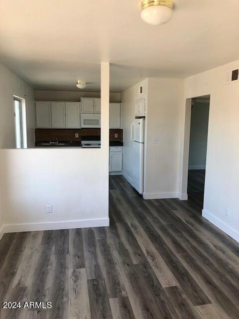 kitchen featuring white appliances, dark wood-type flooring, baseboards, white cabinets, and dark countertops