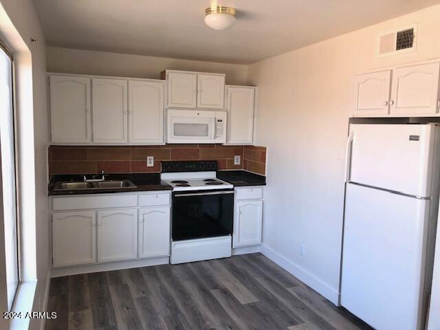 kitchen featuring white appliances, visible vents, dark countertops, white cabinetry, and a sink