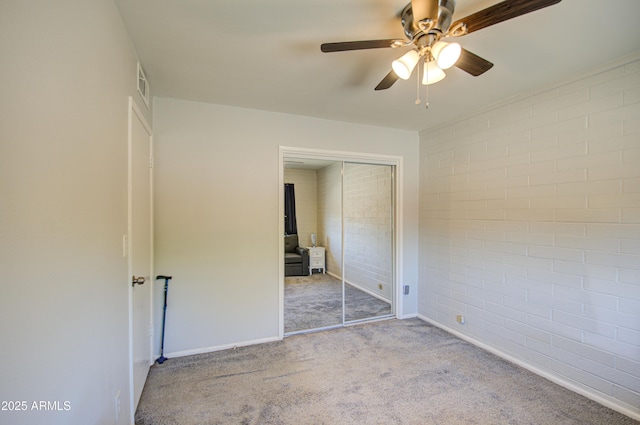 unfurnished bedroom featuring visible vents, brick wall, ceiling fan, carpet, and a closet