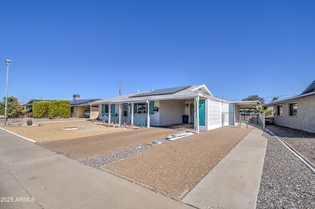 view of front of property featuring covered porch, concrete driveway, roof mounted solar panels, fence, and an attached carport