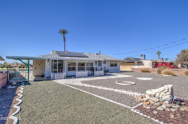 view of front of house with a sunroom, roof mounted solar panels, a gate, and fence