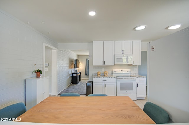 kitchen featuring white appliances, light tile patterned floors, brick wall, white cabinetry, and recessed lighting