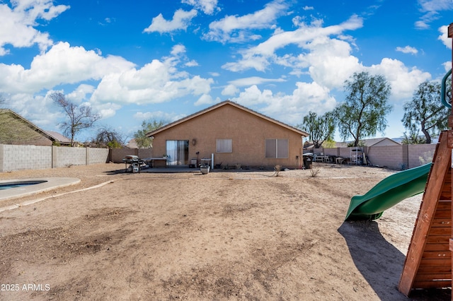 rear view of property with a playground, fence, and stucco siding