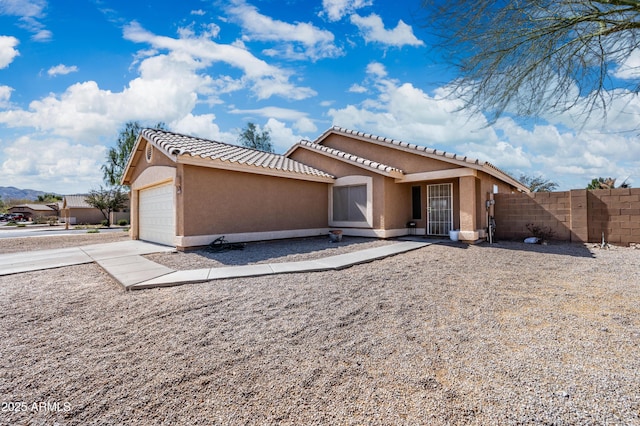 view of front of property with an attached garage, fence, driveway, a tiled roof, and stucco siding