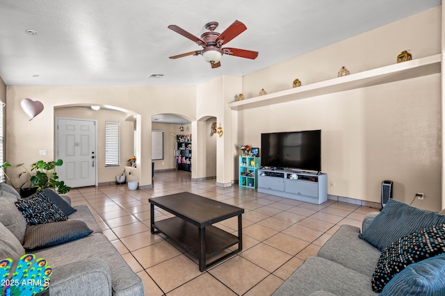 living area featuring arched walkways, light tile patterned floors, visible vents, ceiling fan, and baseboards