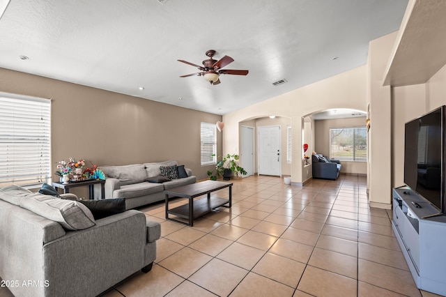 living area with light tile patterned floors, visible vents, arched walkways, baseboards, and a ceiling fan