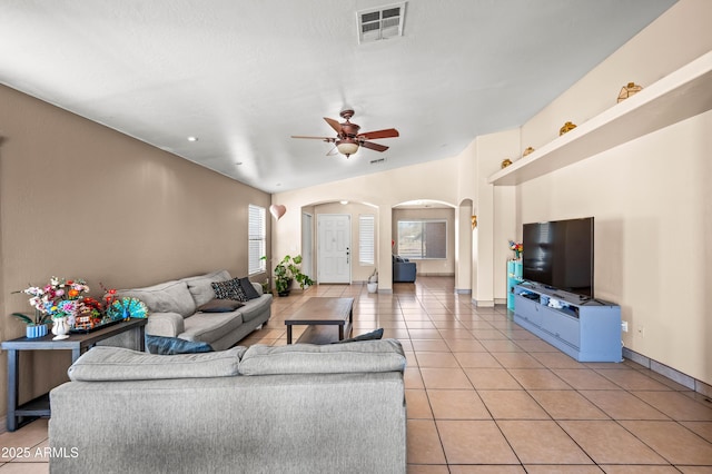 living room featuring arched walkways, ceiling fan, light tile patterned floors, visible vents, and vaulted ceiling