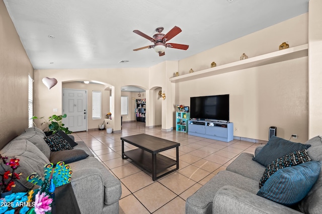 living area with arched walkways, lofted ceiling, a ceiling fan, light tile patterned flooring, and baseboards