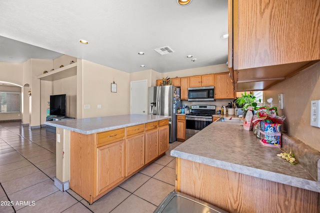 kitchen with light tile patterned floors, arched walkways, a kitchen island, appliances with stainless steel finishes, and light countertops