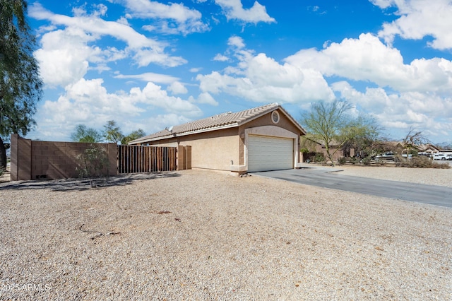 view of side of property with a tile roof, stucco siding, concrete driveway, fence, and a garage