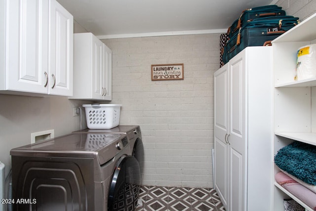 laundry area with brick wall, washing machine and dryer, and cabinets