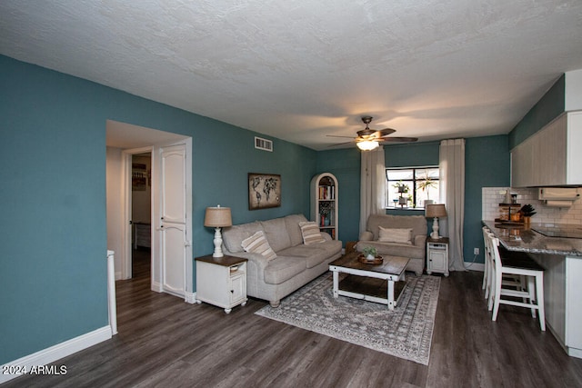 living room with a textured ceiling, dark wood-type flooring, and ceiling fan