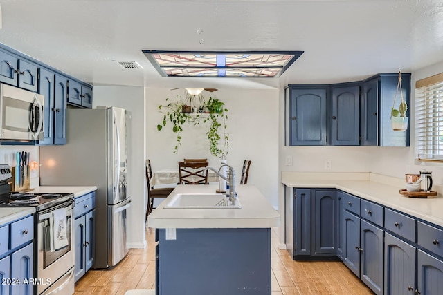 kitchen with appliances with stainless steel finishes, a kitchen island with sink, blue cabinetry, light hardwood / wood-style flooring, and sink