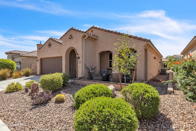 mediterranean / spanish home with driveway, a tile roof, central air condition unit, stucco siding, and a garage