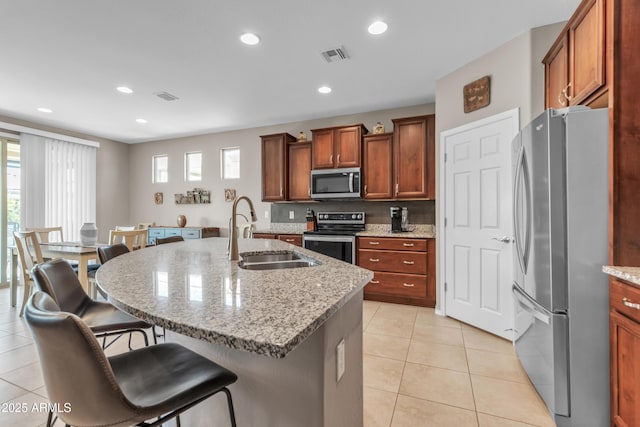 kitchen with light tile patterned flooring, a sink, a kitchen breakfast bar, appliances with stainless steel finishes, and visible vents