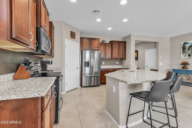 kitchen featuring light tile patterned flooring, a sink, a breakfast bar, appliances with stainless steel finishes, and visible vents