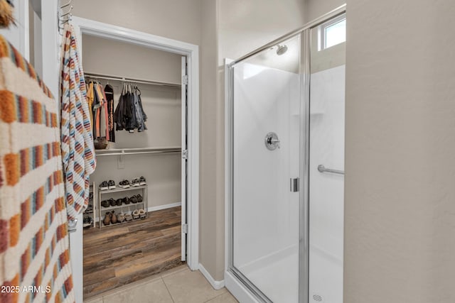 full bath featuring a stall shower, tile patterned floors, baseboards, and a spacious closet