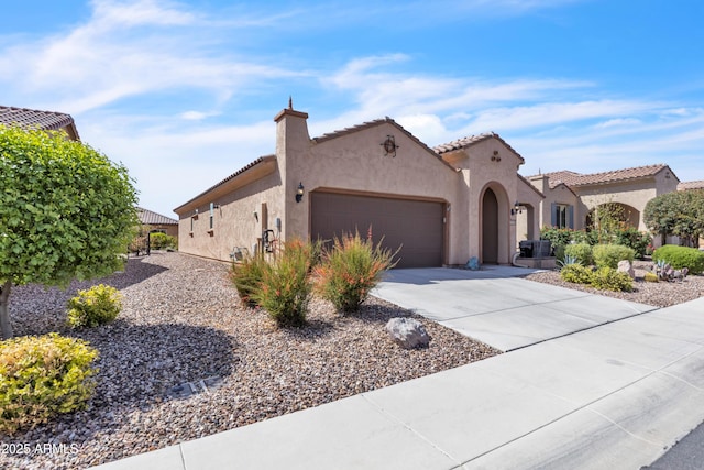 mediterranean / spanish house with stucco siding, a tiled roof, a garage, and concrete driveway