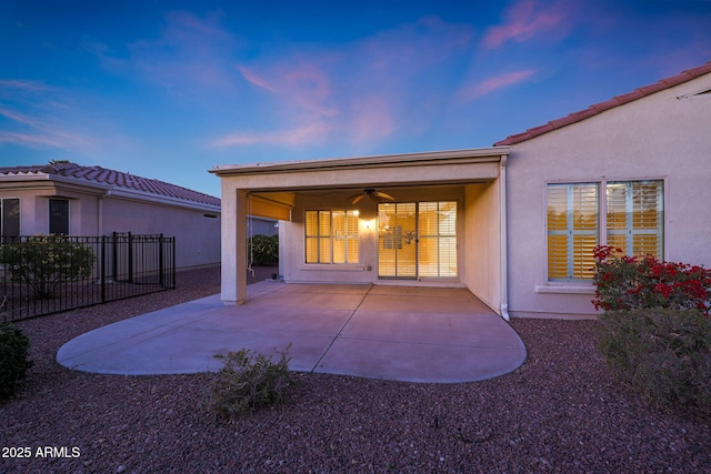 back house at dusk featuring ceiling fan and a patio area